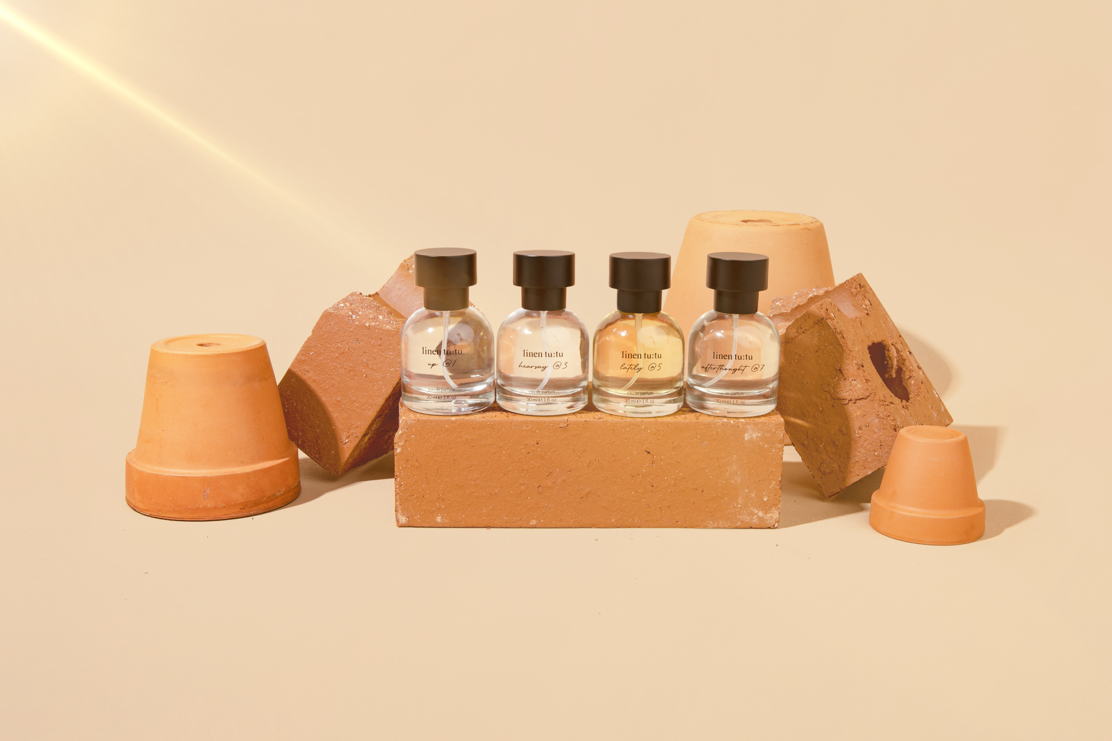 Four Linen Tutu fragrances in line on top of a terracotta brick, surrounded by terracotta pots